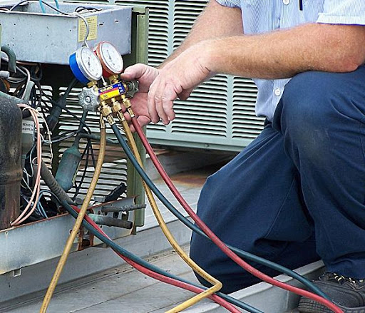 Technician using manifold gauges to inspect a rooftop AC unit during a seasonal tune-up in the Fort Worth area